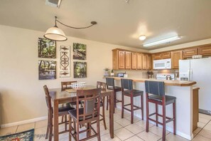 A kitchen with wooden cabinets, a dining table with chairs, a pendant light, and a microwave.