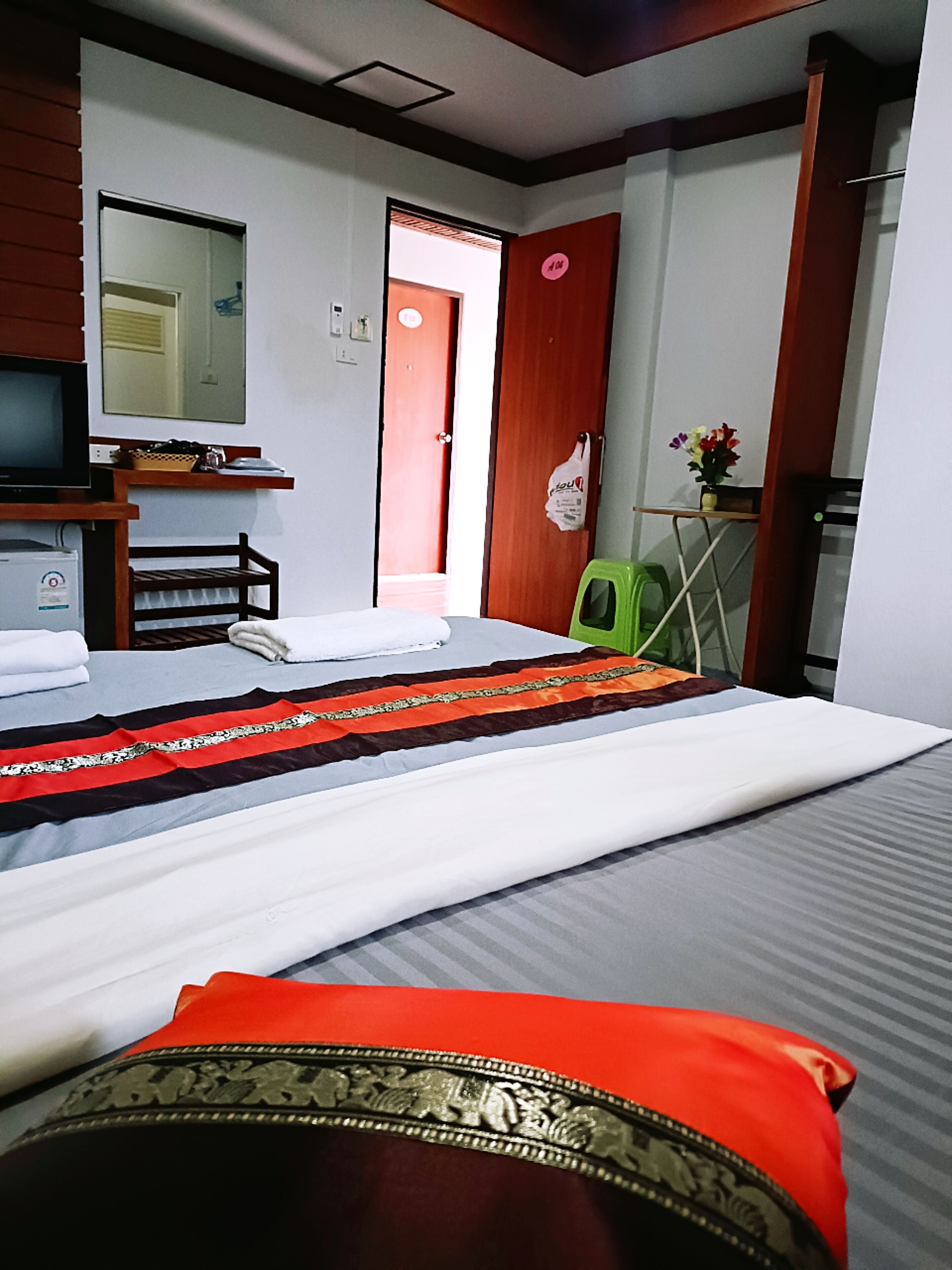 A hotel room with a bed, a desk with a computer, a chair, a small table with a vase of flowers, and a door.