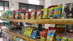 Un rayon d’épicerie où les étagères sont remplies de divers produits emballés, notamment des en-cas, des chips et de l’eau en bouteille.