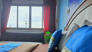 Un lit donnant sur une tour, visible à travers une fenêtre, avec une plante et un oreiller bleu.