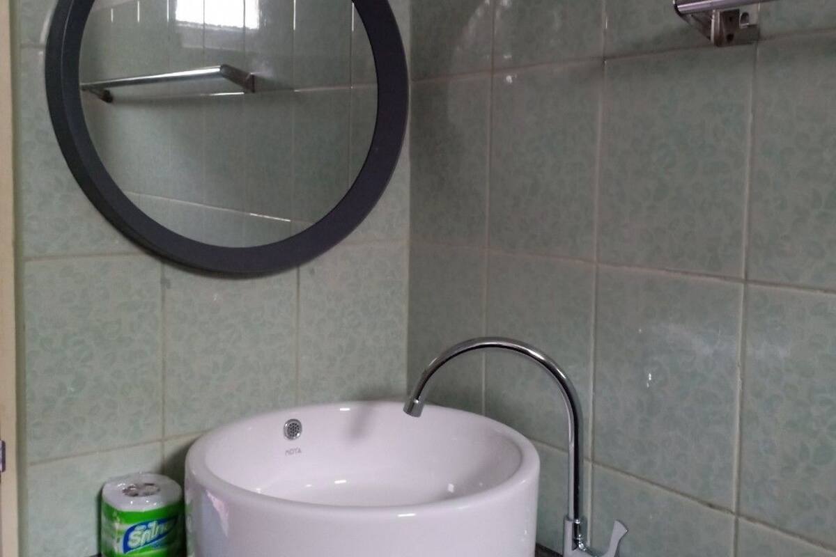 A bathroom with a round mirror, a white sink, and green tiled walls.