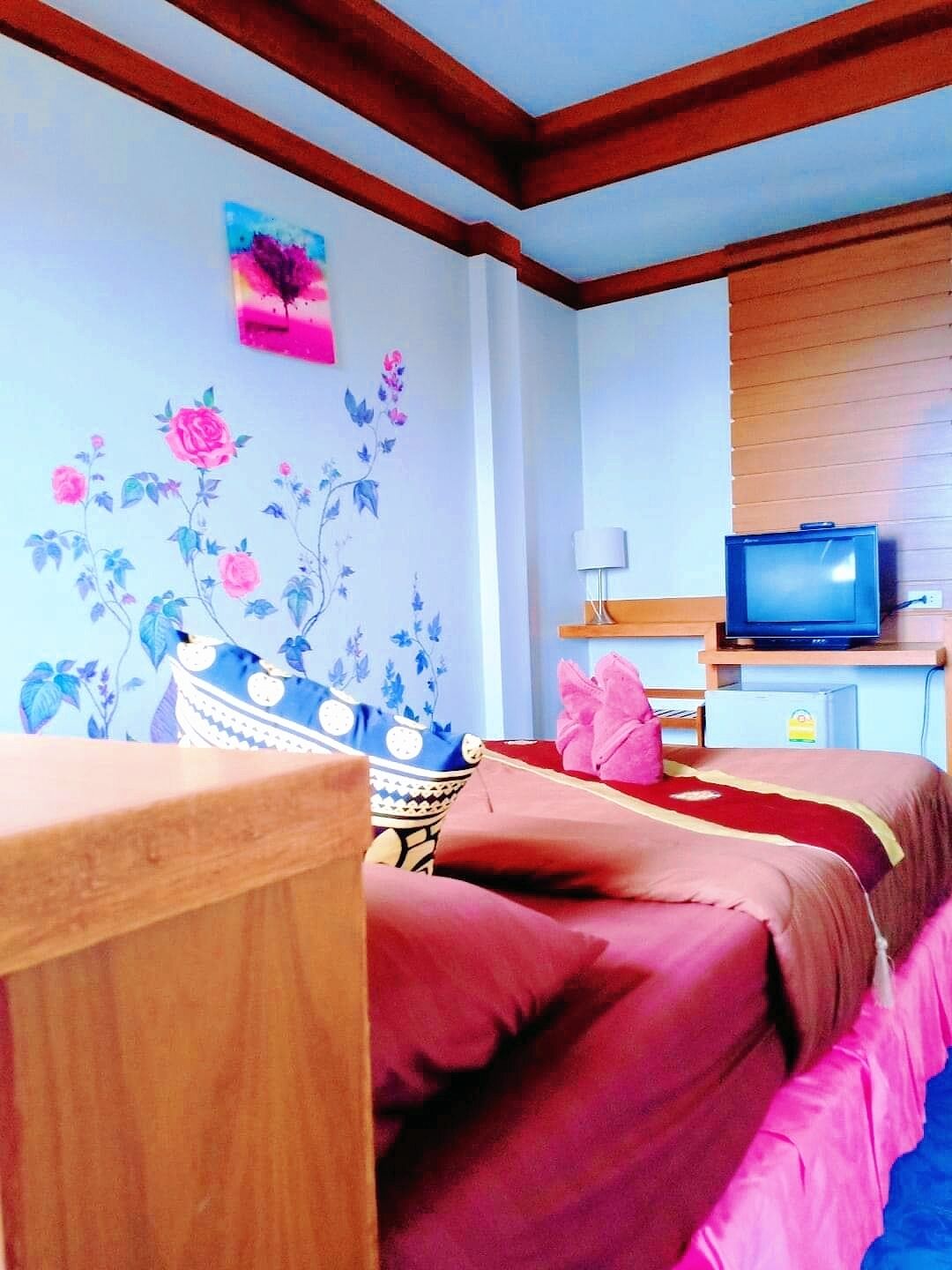 Habitación de hotel con dos camas, un televisor y una pared con papel tapiz floral.