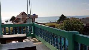 Un balcon donnant sur la mer, agrémenté de bancs en bois et d’une rambarde verte.