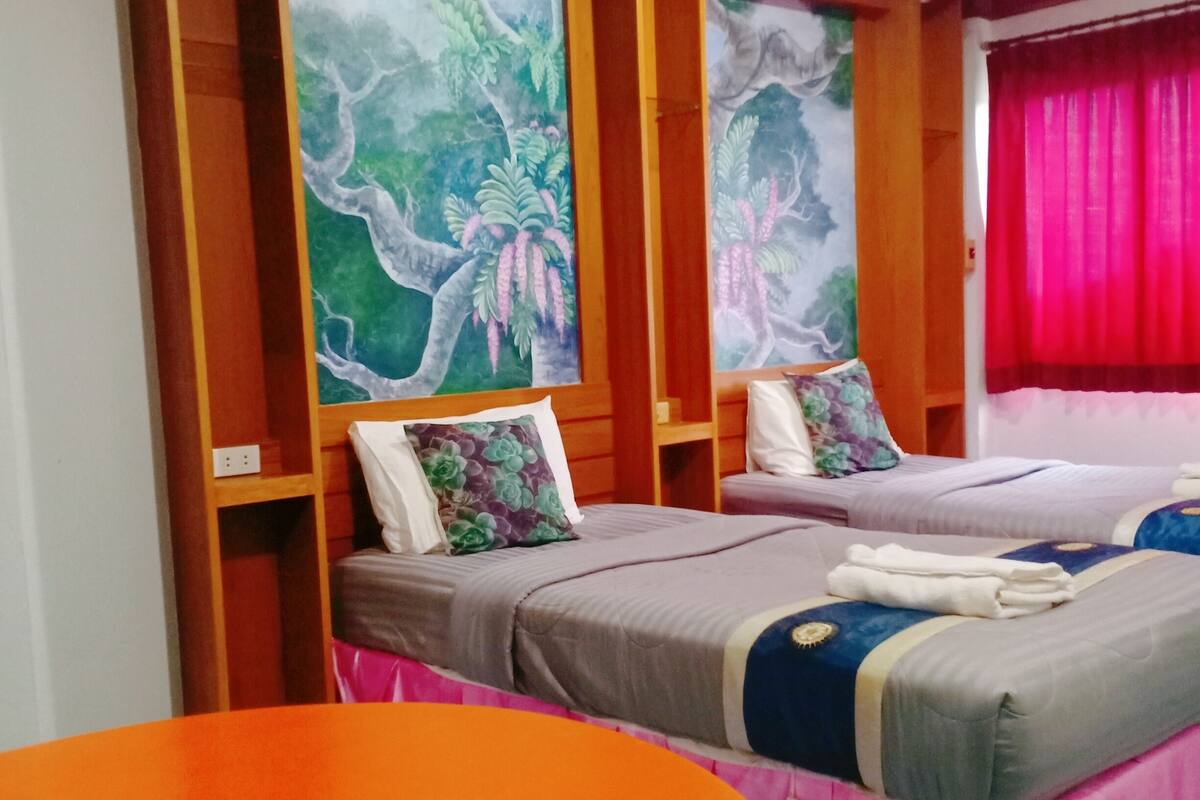 A room with two beds, a wooden headboard, a red curtain, and a table with plates.