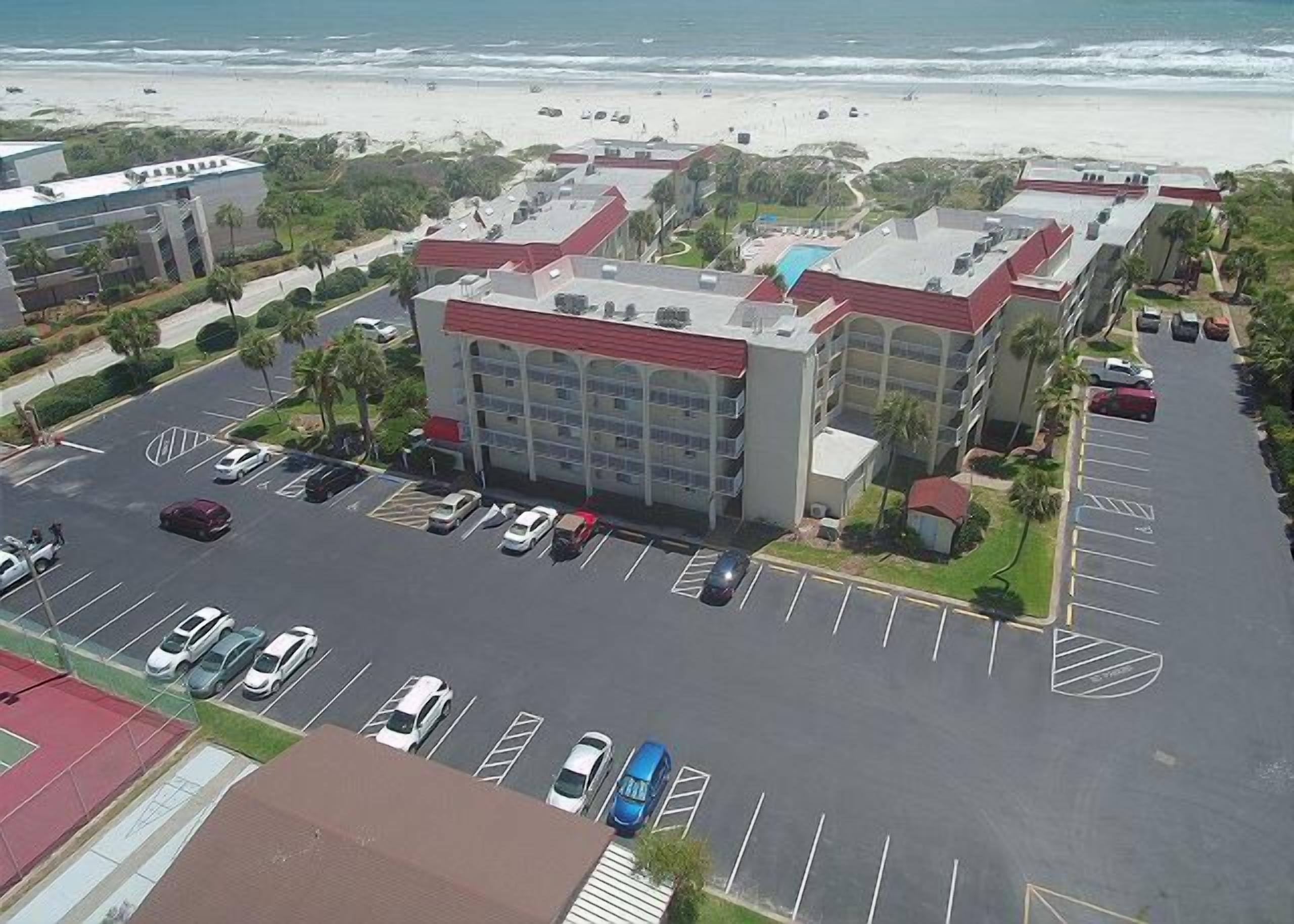 A multi-story hotel with a parking lot in front, located near a beach.