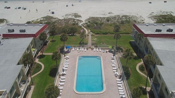 Un hotel con piscina rodeada de sillas de descanso, vista a la playa y zona de estacionamiento.