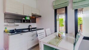 Uma cozinha moderna com armários brancos, bancada preta e um espaço de jantar com mesa branca e cadeiras verdes.