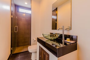 Une salle de bain moderne avec un lavabo en forme de bol en verre, une douche à l’italienne et un grand miroir.