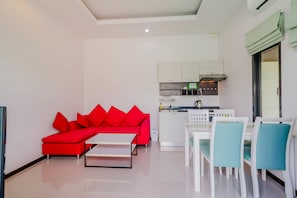 A modern living room with a red sofa, a white coffee table, and a dining area with white chairs. - Tropical Pool Villas near Phuket Zoo (Chalong)