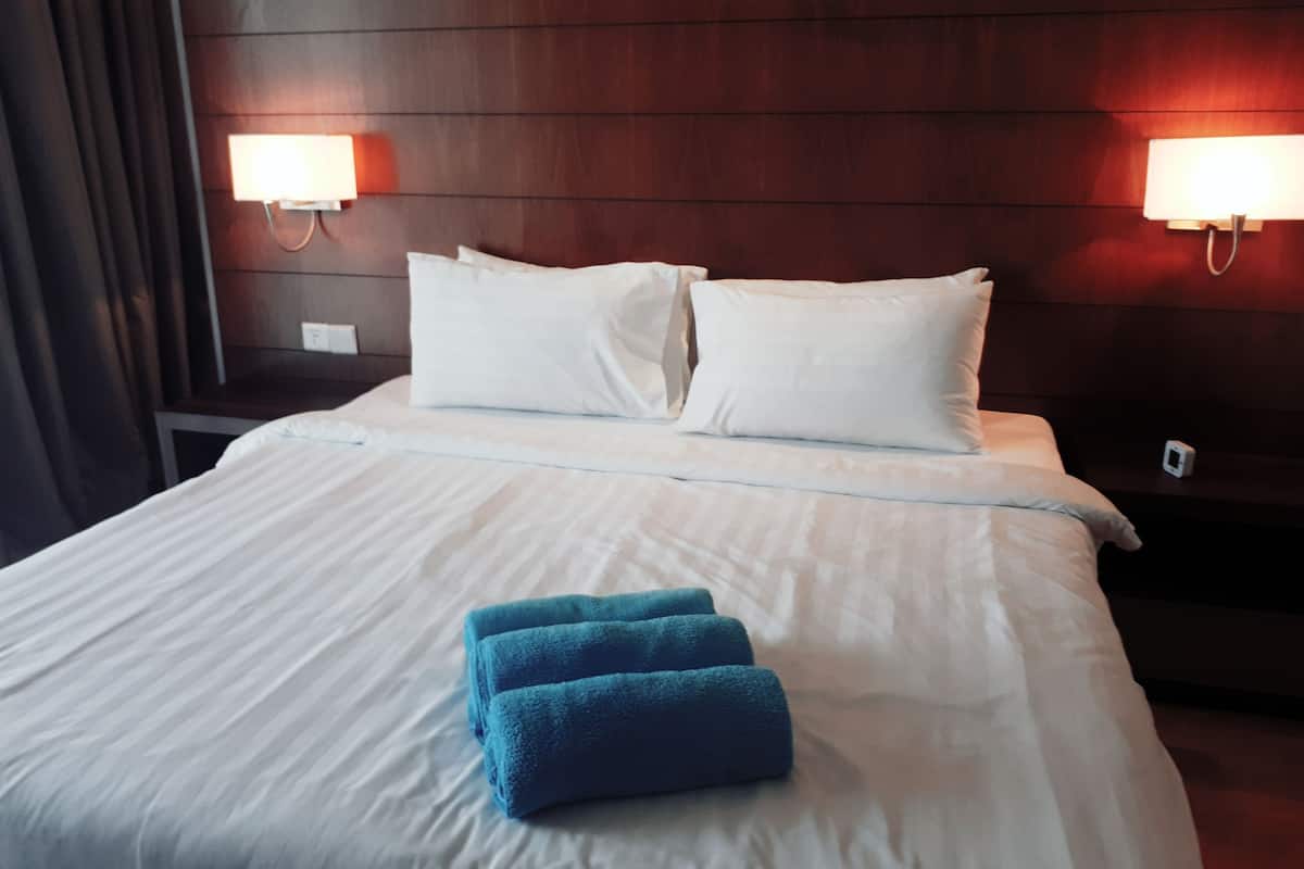 Ein Hotelzimmer mit einem ordentlich bezogenen Bett, zwei Nachttischlampen und einem Nachttisch mit Telefon.