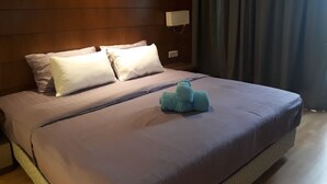 A neatly made bed with a light-colored duvet, a single blue plush toy, and a wooden headboard. - Greystone Haus at D' Majestic Place (Kuala Lumpur)