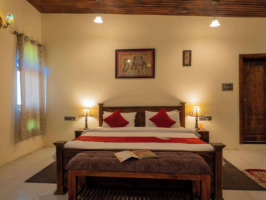 A neatly arranged bedroom with a wooden bed, two bedside lamps, a framed picture on the wall, and a wooden door.