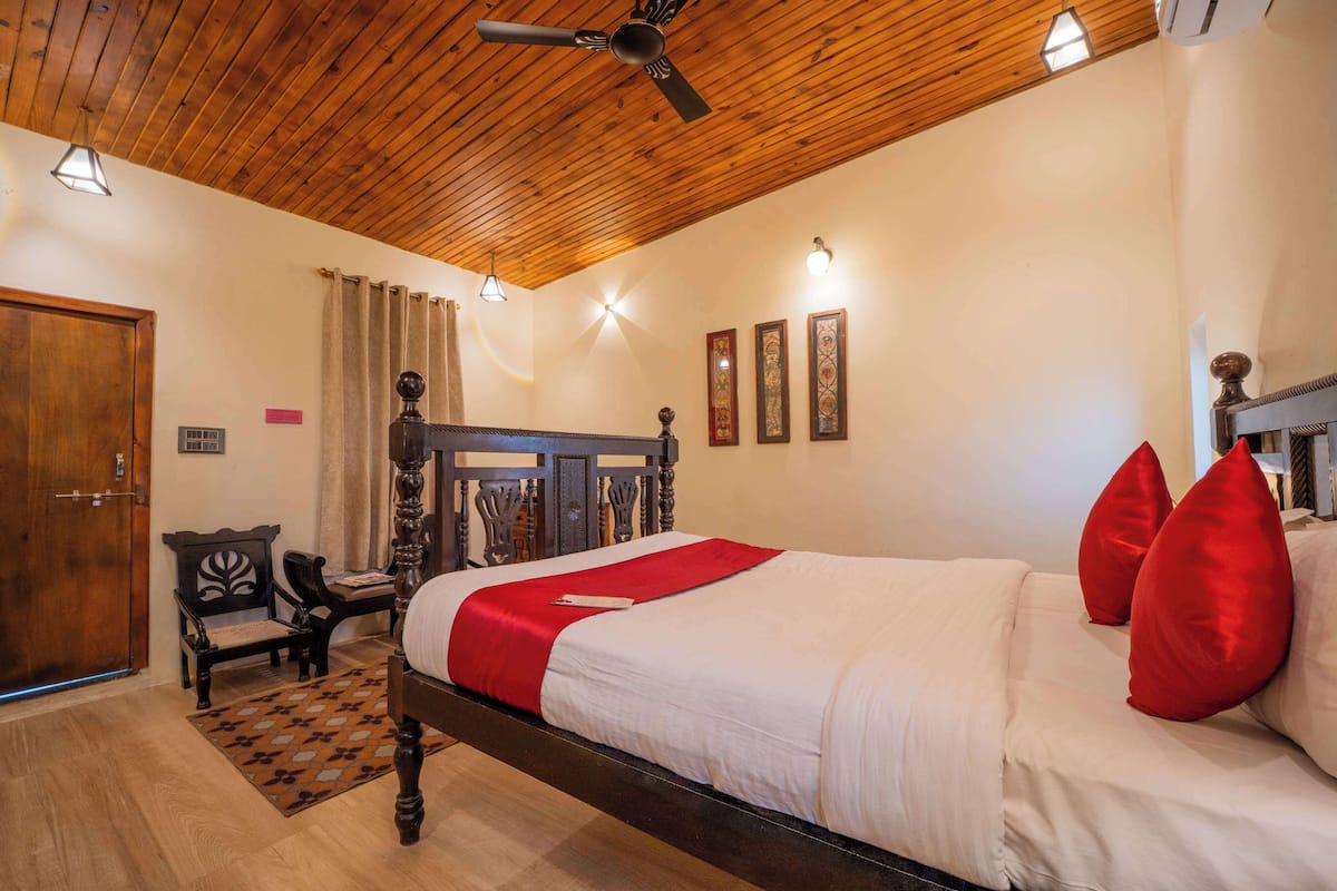 Een slaapkamer met een houten plafond, een bed met rode kussens, een houten bankje en een kleine tafel.