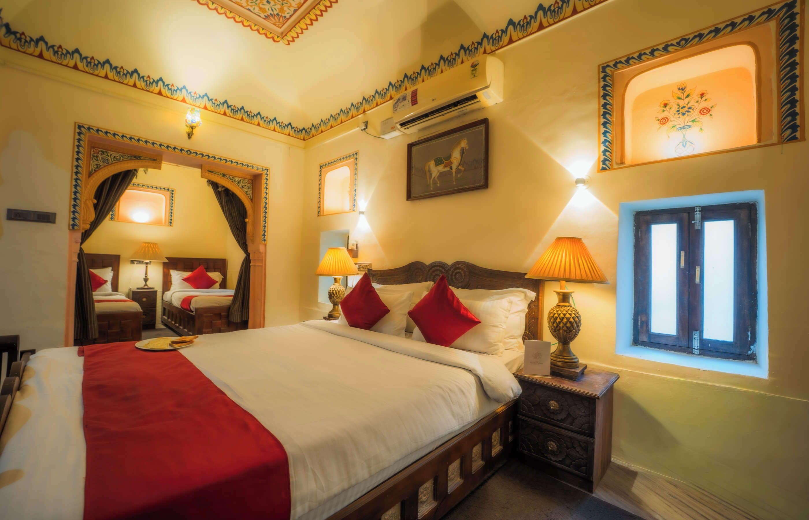 A hotel room with a large bed, two bedside tables, a nightstand, a window with curtains, and decorative wall art.