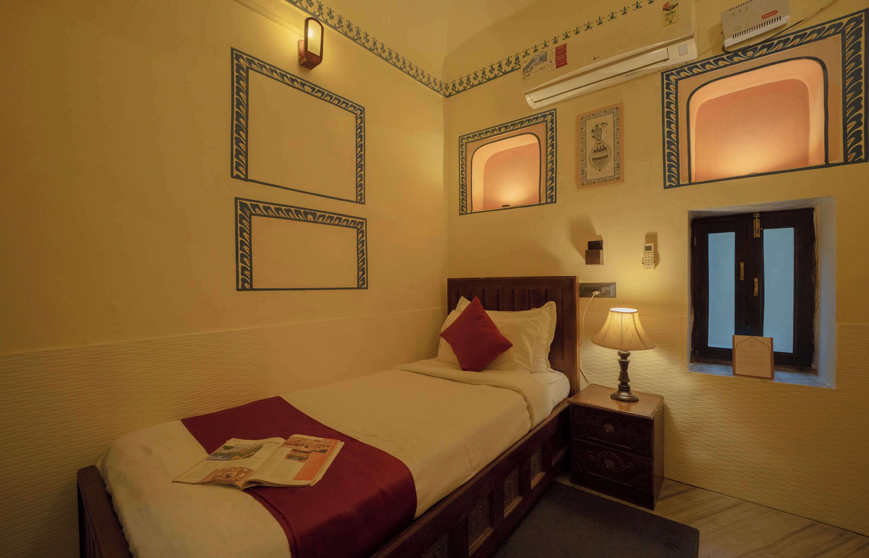 A hotel room with a neatly made bed, a bedside table with a lamp, and decorative wall mirrors.