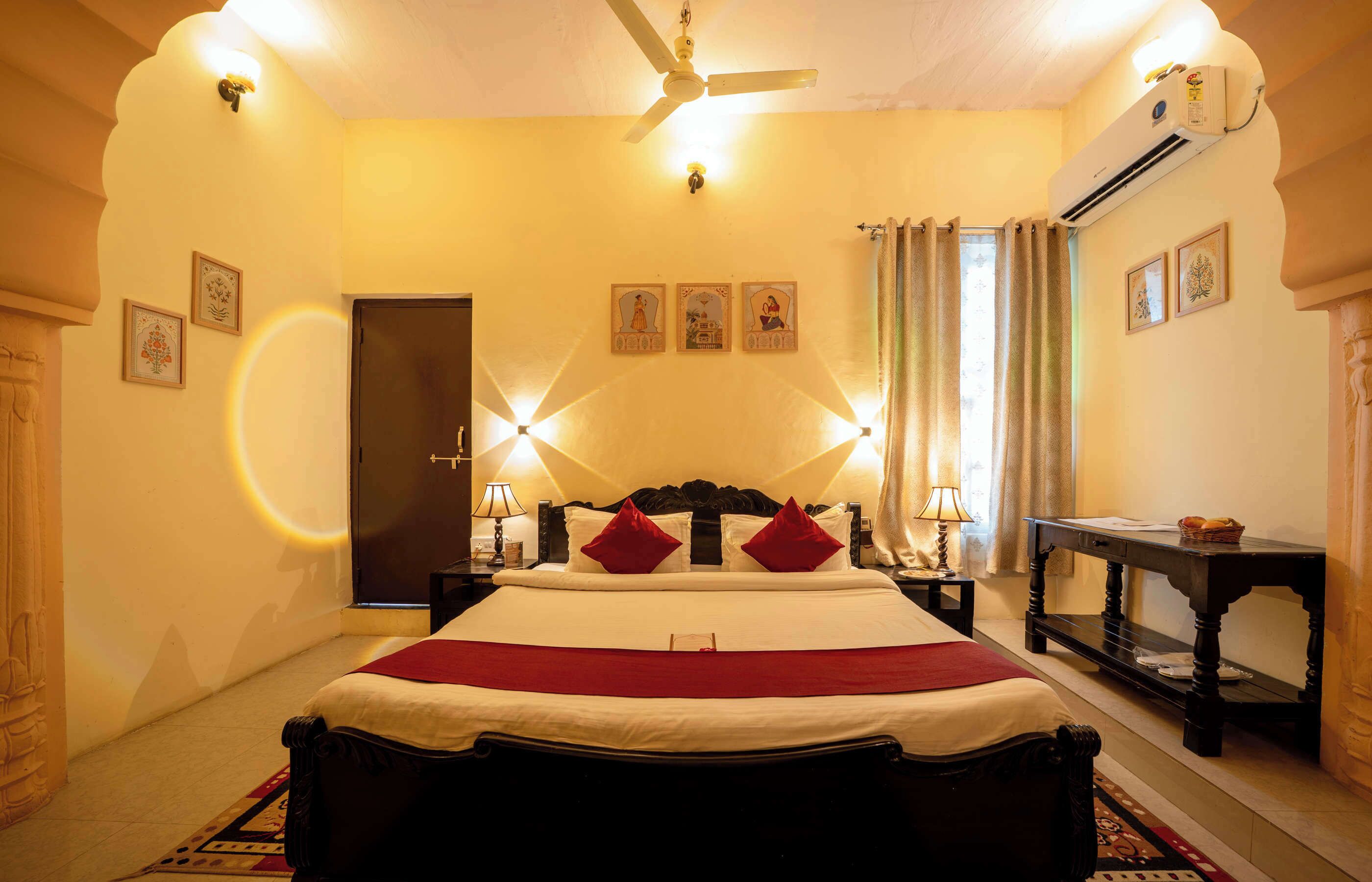 Une chambre bien éclairée, dotée d’un grand lit, d’un ventilateur de plafond et d’un appareil de climatisation.