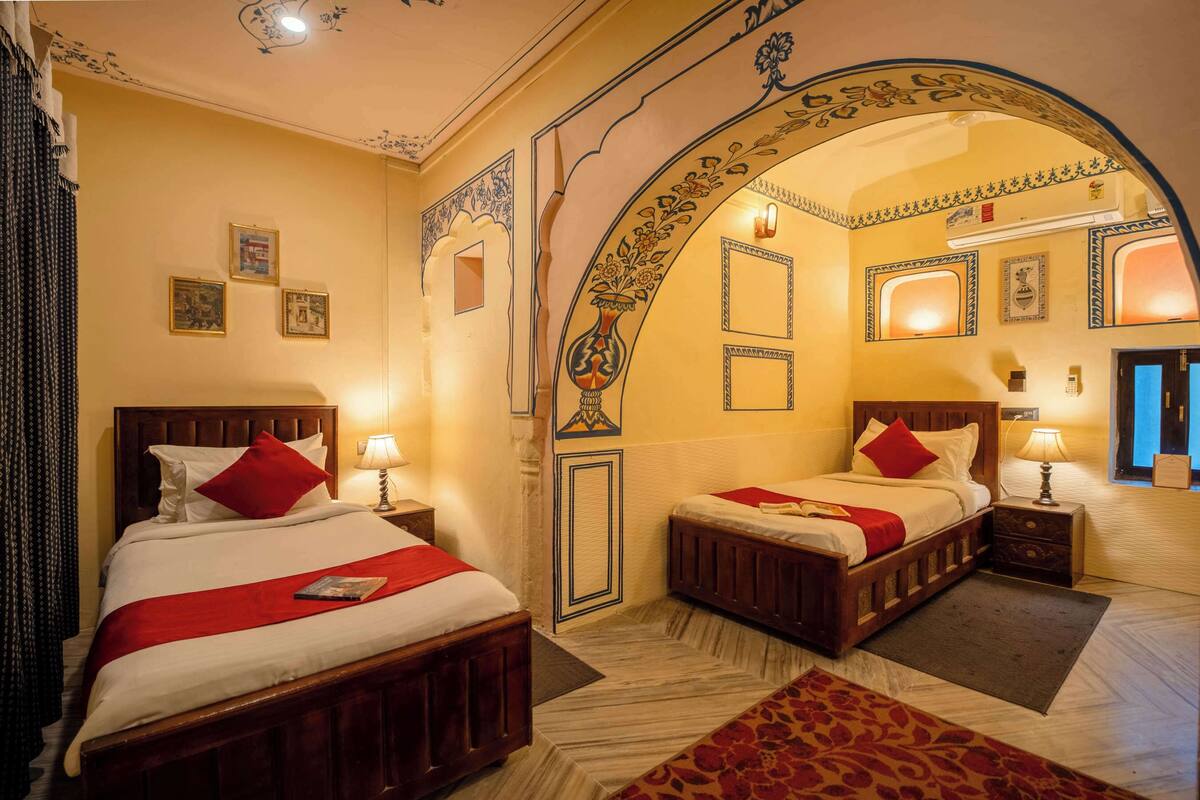 Een hotelkamer met twee bedden, een decoratieve boog en een klein zithoekje.