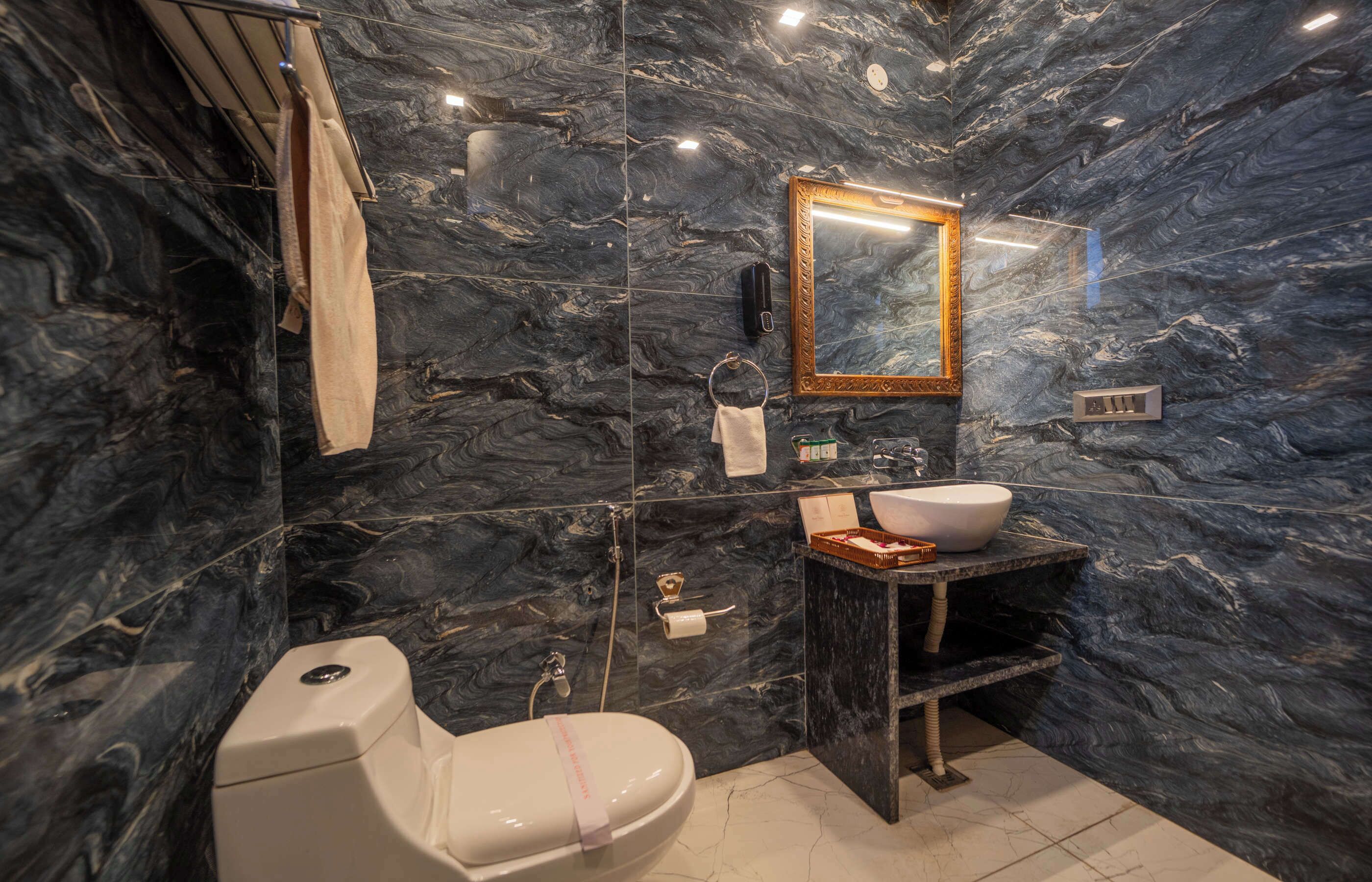 Un baño con pared de mármol, lavamanos, inodoro y espejo.