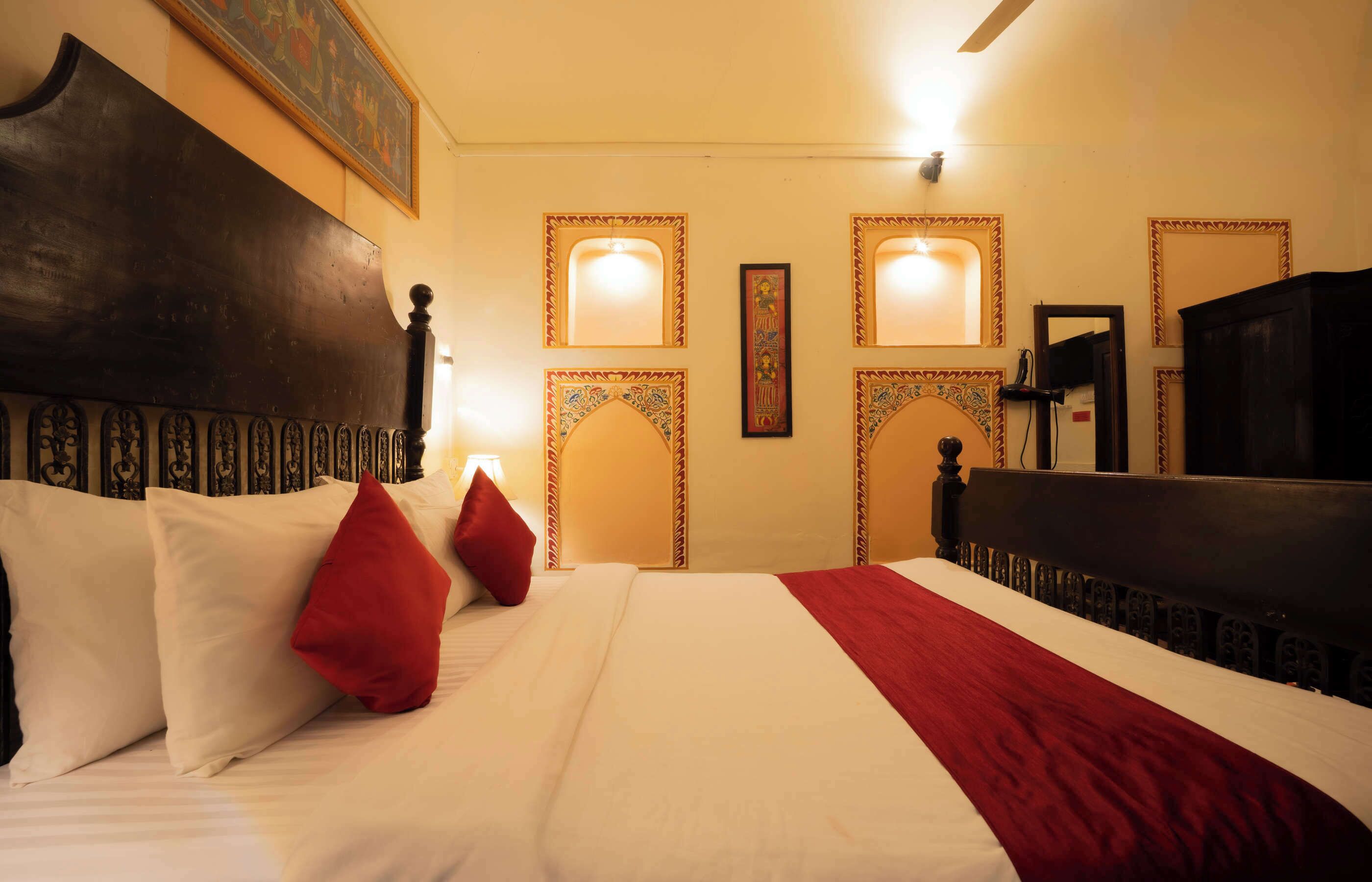 A hotel room with a large bed, a wooden headboard, and decorative wall sconces.