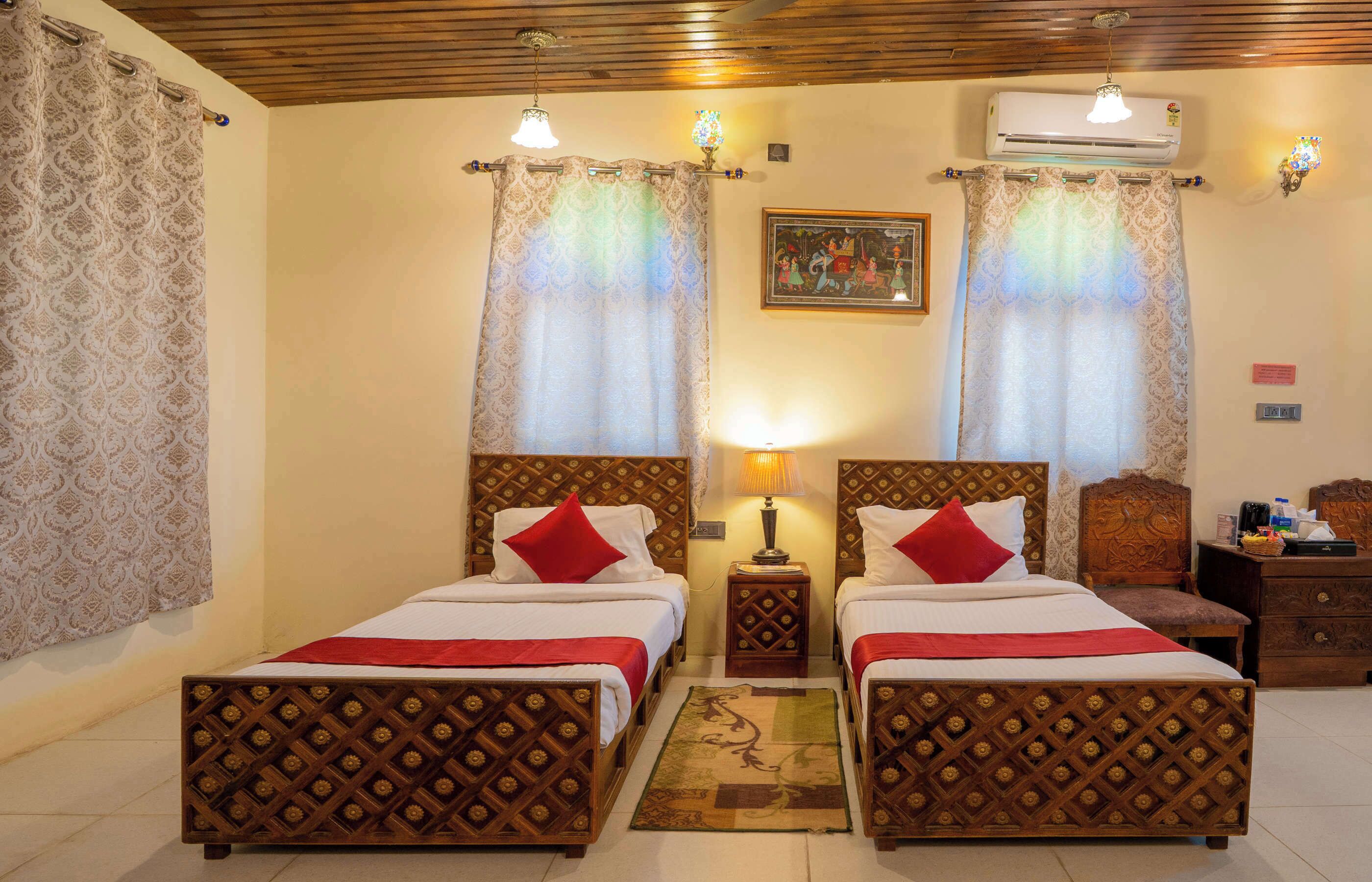 Habitación de hotel con dos camas, cabecera de madera, mesita de noche, lámpara y unidad de aire acondicionado.