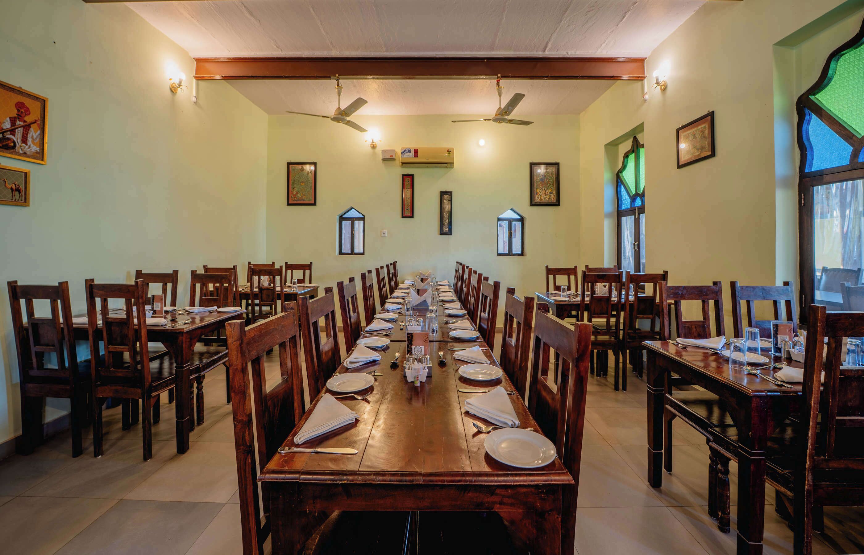 A long dining table with chairs, ceiling fans, and framed pictures on the walls.