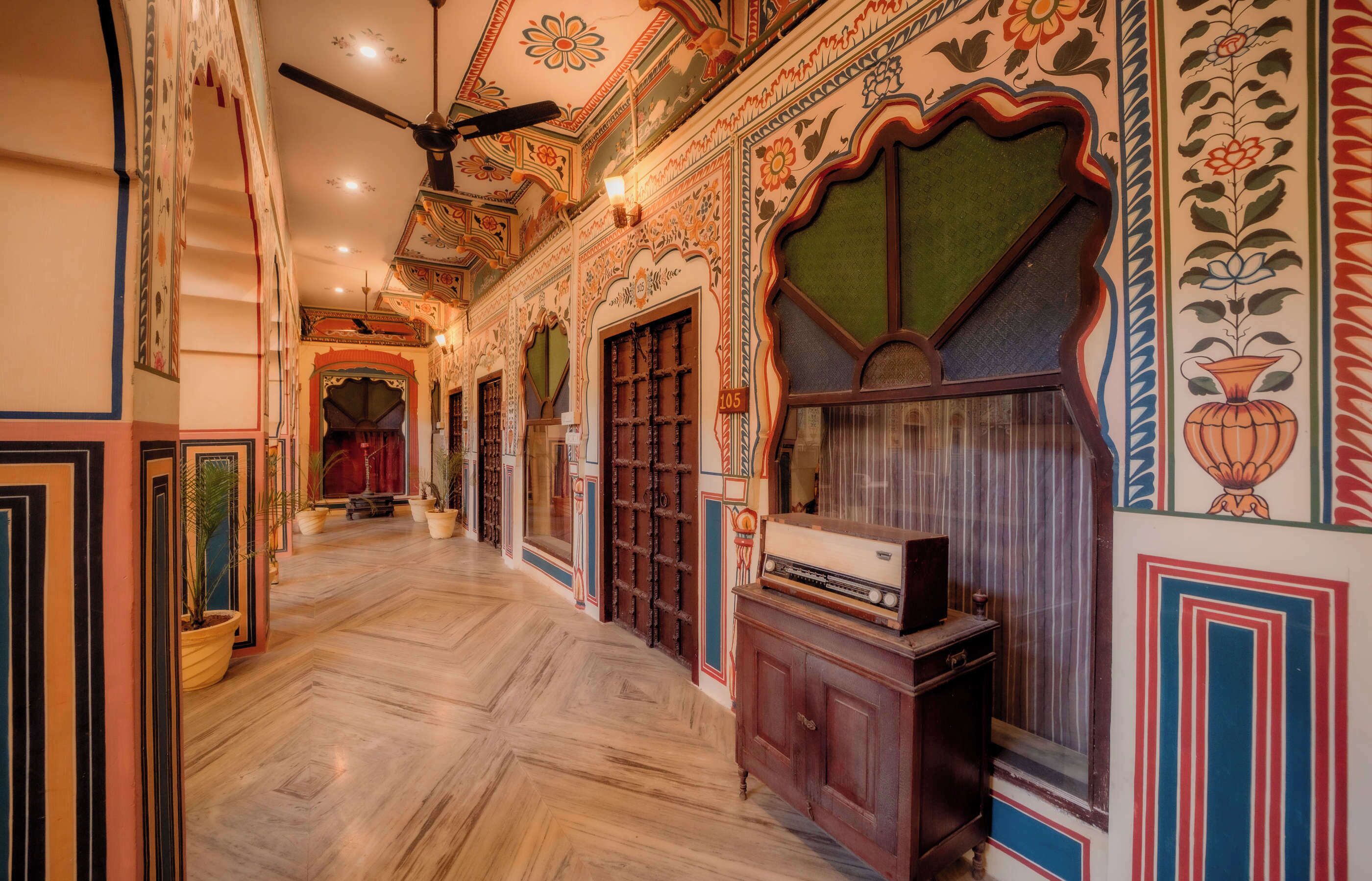 Un couloir orné de motifs décoratifs sur les murs, avec un ventilateur de plafond et une radio ancienne posée sur un meuble.