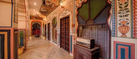 A hallway with ornate wall designs, a ceiling fan, and a vintage radio on a cabinet.