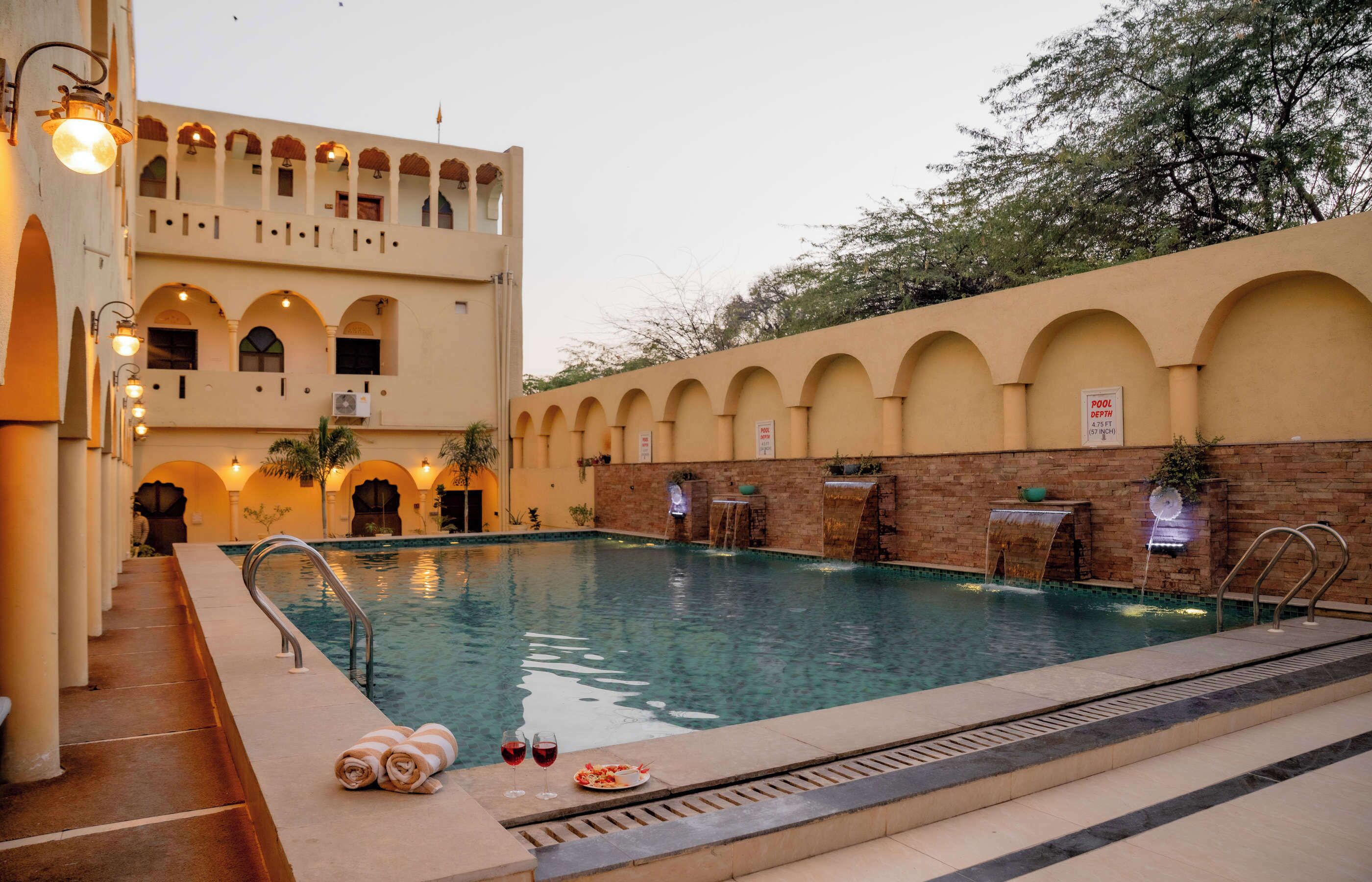 Uma área de piscina com vista desobstruída, espaço para relaxar e um edifício com janelas em arco e uma placa indicando um bar na piscina.