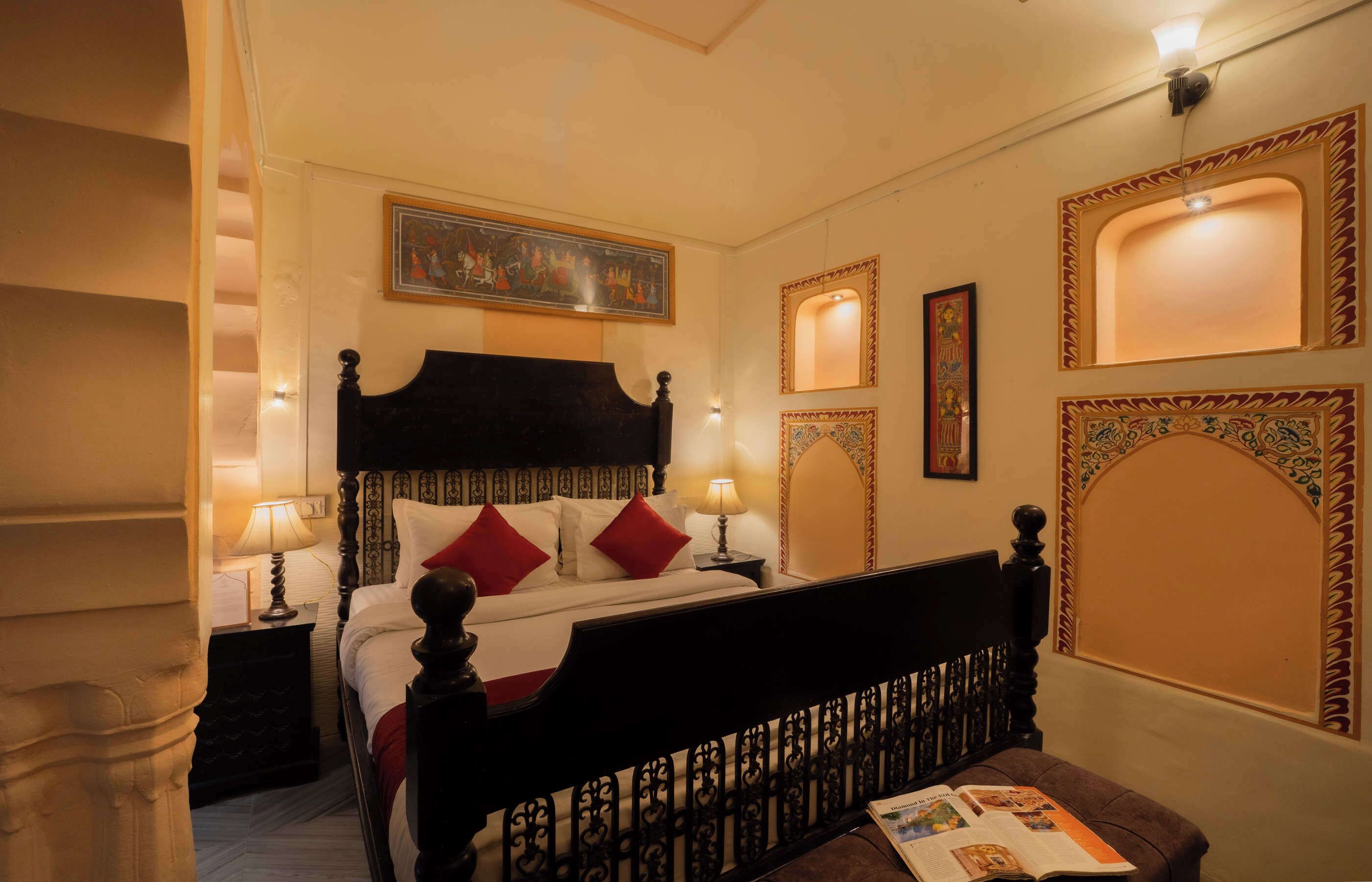 A hotel room with a large bed, two bedside tables, a nightstand, and a reading bench.