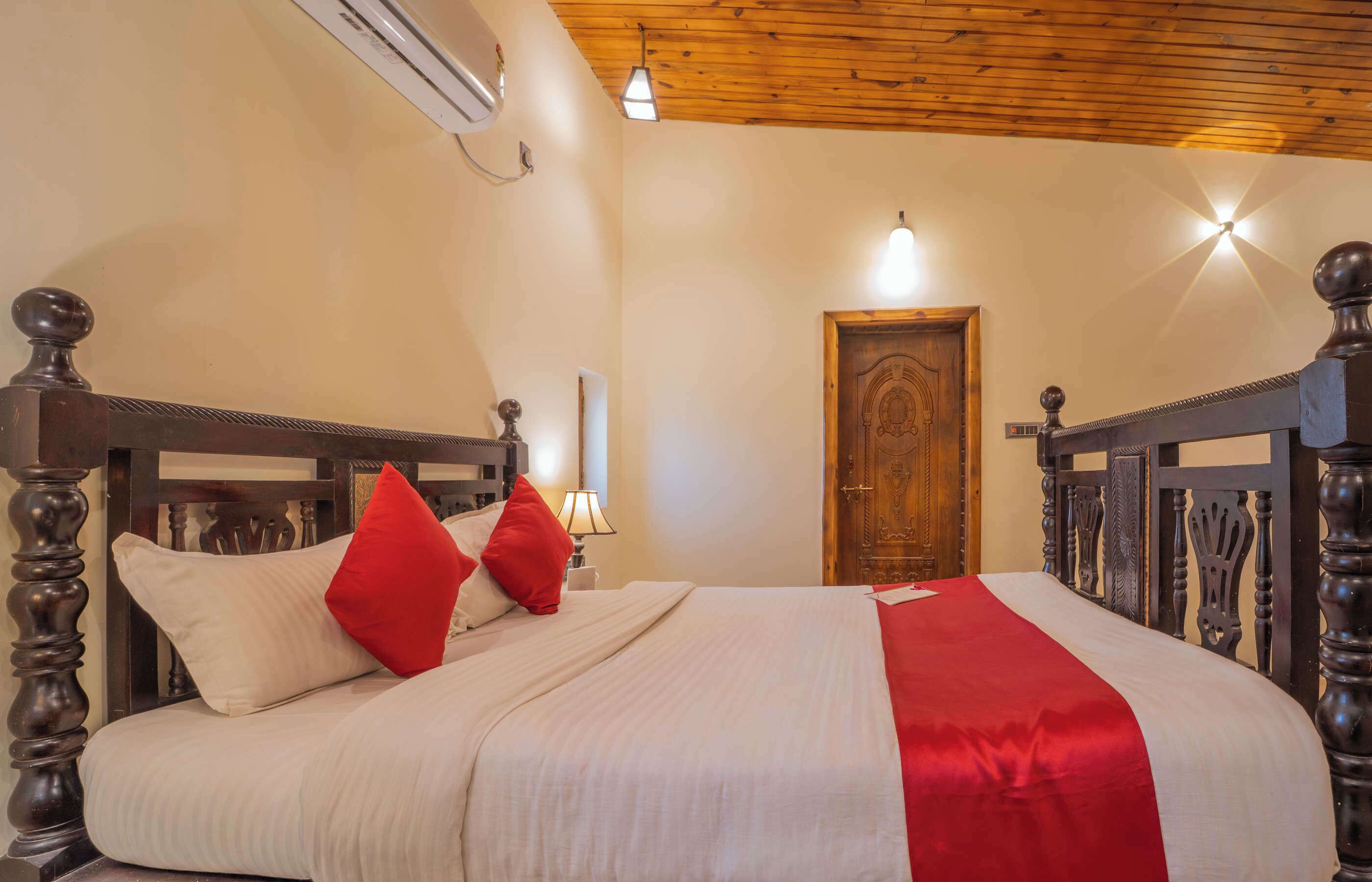 A neatly made bed with a wooden headboard, a red pillow, and a white bedspread.