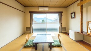 Una habitación con tatami, una mesa, sillas, un refrigerador y vistas a montañas a través de un puertas correderas.