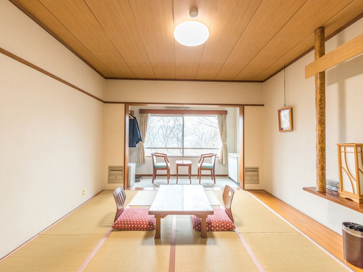 Una tradizionale stanza giapponese con pavimento in tatami, un tavolino in legno e una porta scorrevole che dà su un balcone.