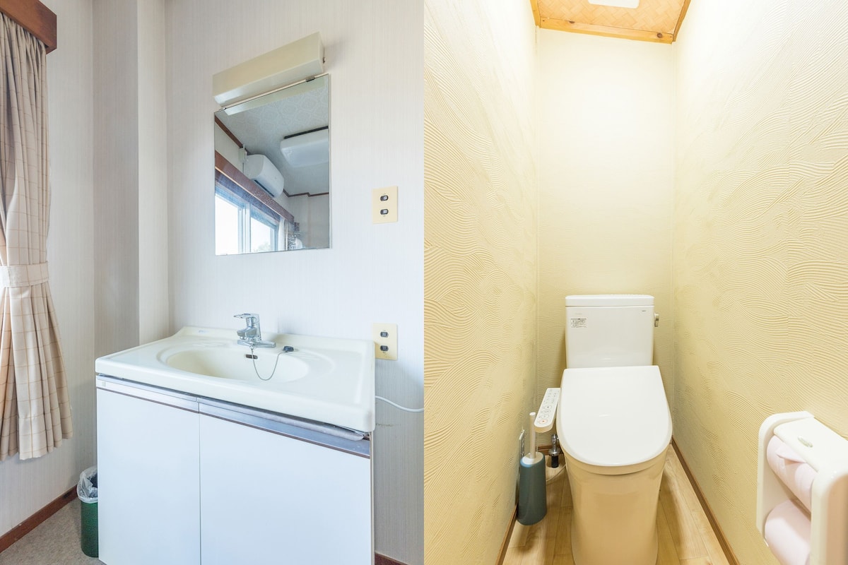 Un baño con lavamanos, espejo, inodoro y dispensador de toallas.