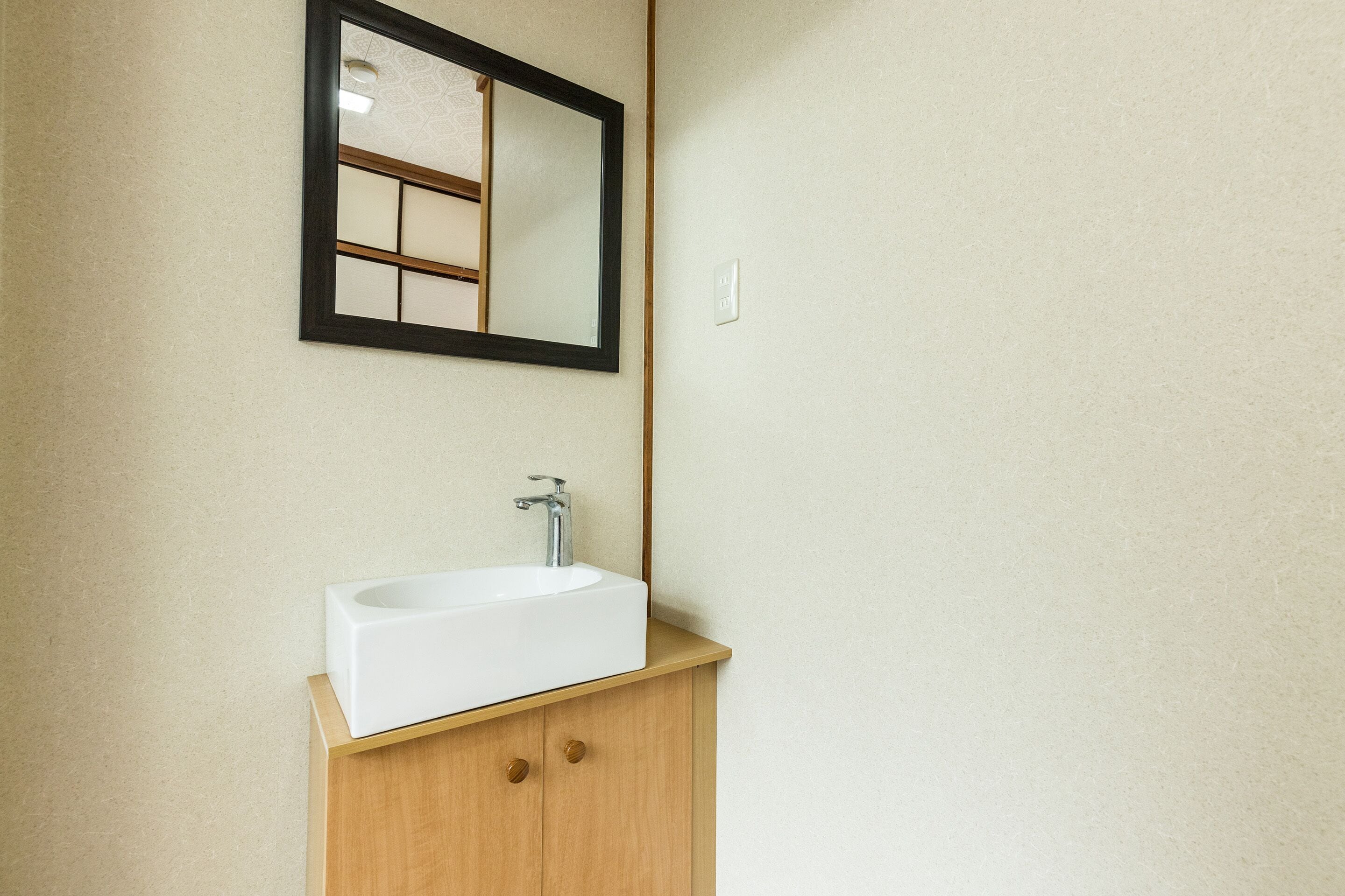 A bathroom with a white sink, wooden cabinet, and a mirror with a black frame.