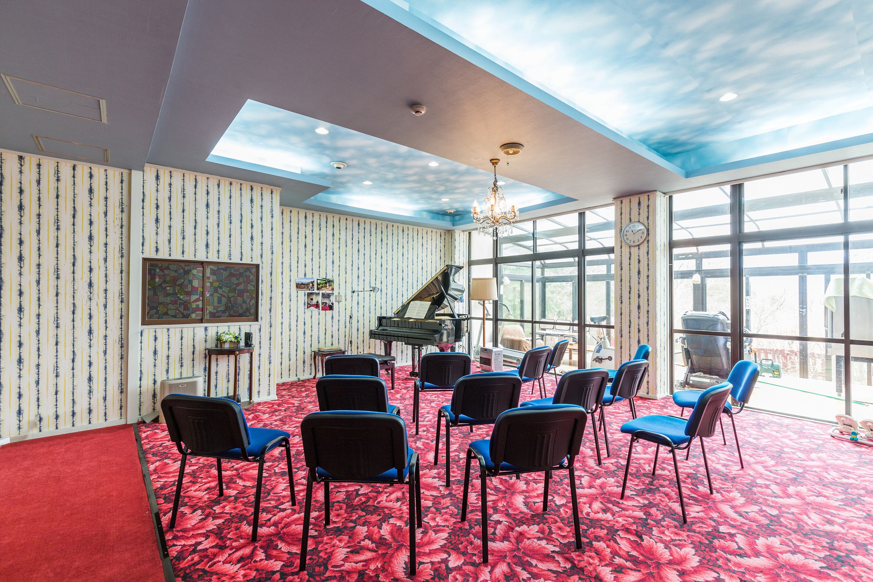 A room with a red carpet, a piano, and multiple chairs arranged for seating.