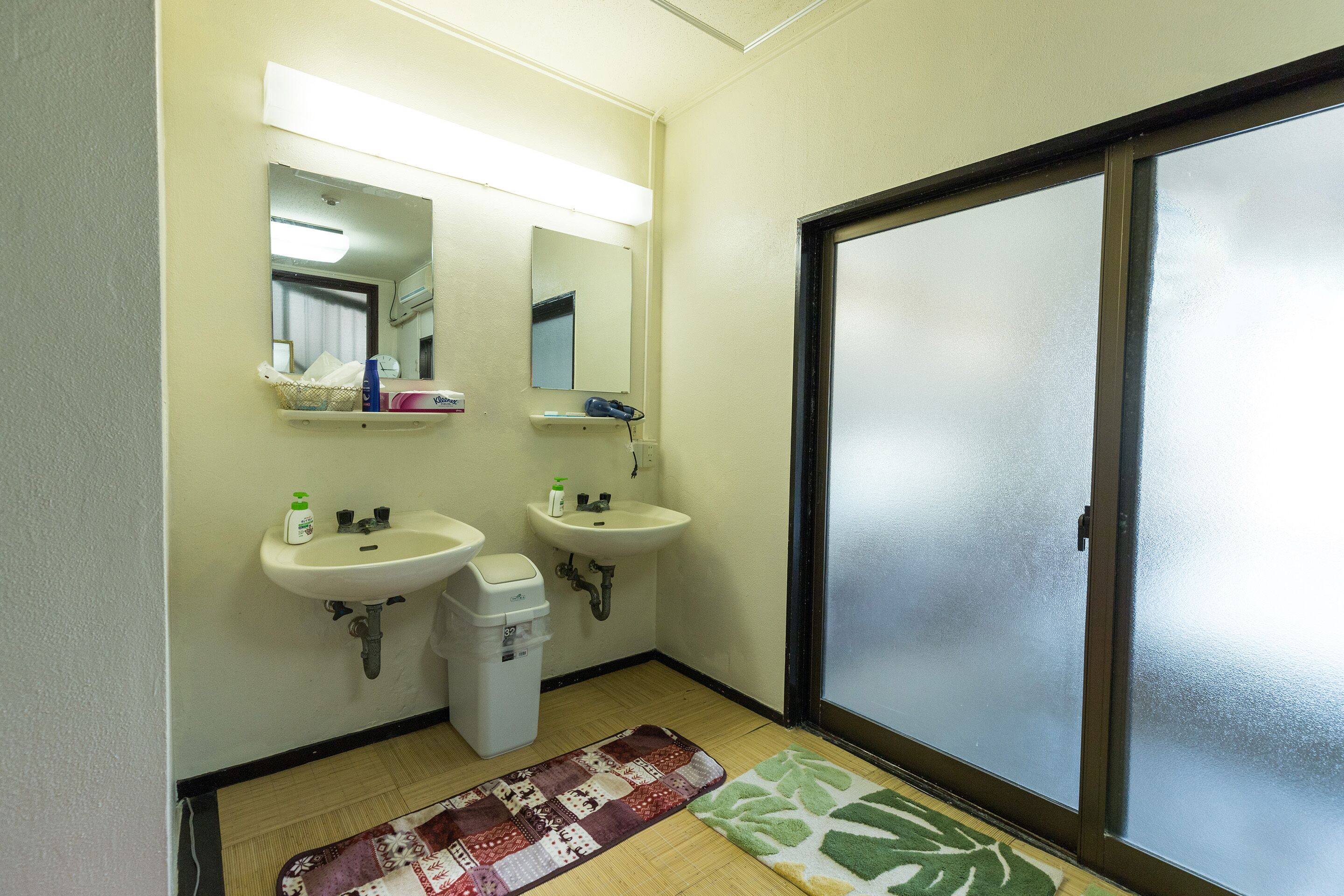 Un baño con dos lavamanos, un espejo y una puerta de vidrio corredera.