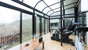 Una habitación moderna con ventanas amplias, una cinta de correr y una mesa de madera con un florero.