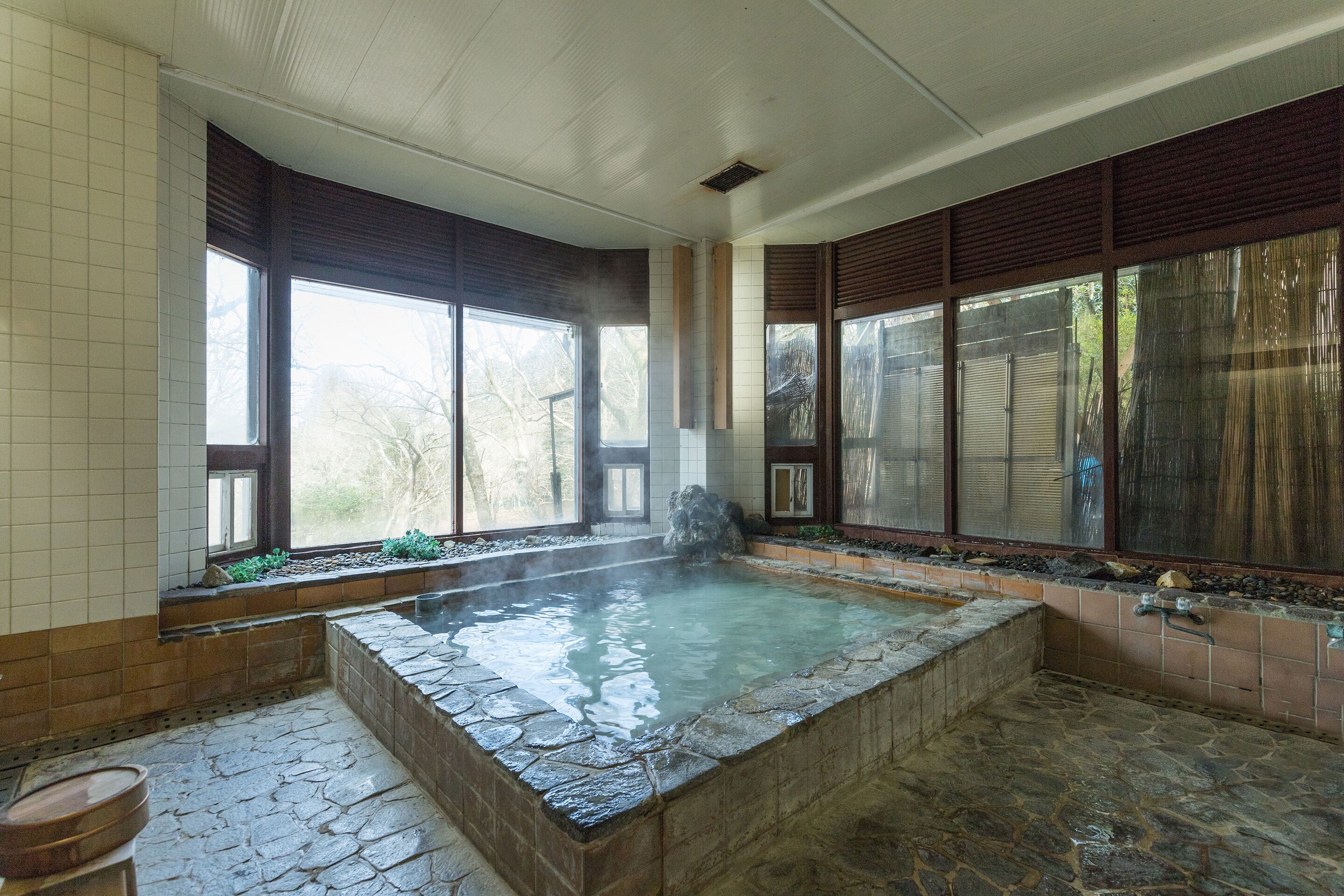 A hot tub area with stone flooring, large windows, and a view of trees.