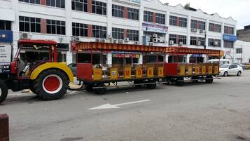 A stationary train with open carriages and a tractor pulling it, parked in front of a building with multiple signs and windows.
