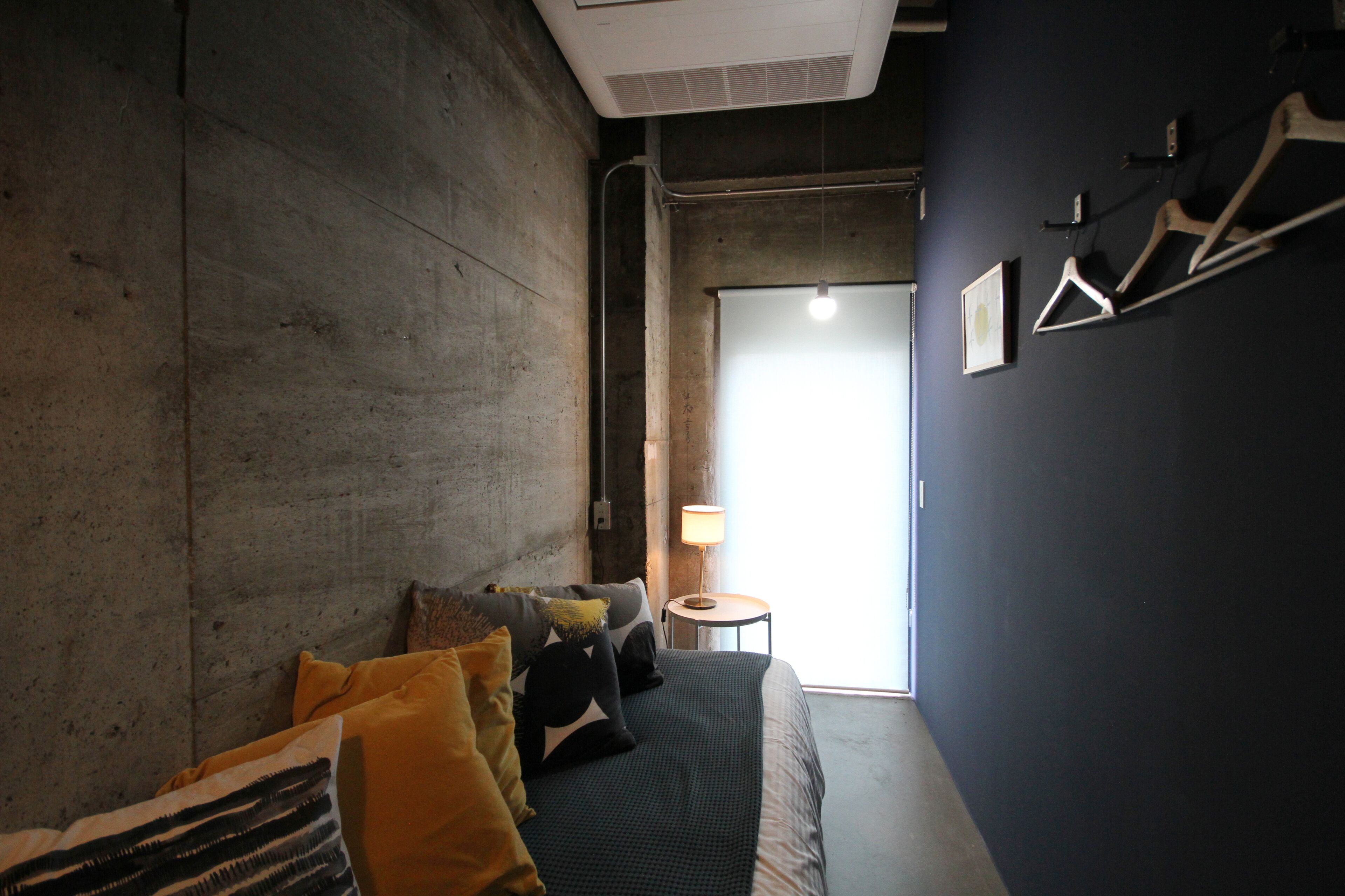 A room with a bed, a small table with a lamp, and a door leading to a bright area.