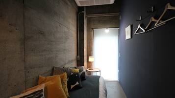 A room with a bed, a small table with a lamp, and a door leading to a bright area.