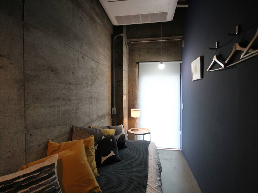 A room with a bed, a small table with a lamp, and a door leading to a bright area.