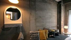 A bedroom with a bed, pillows, a round mirror, and a small table with a lamp. - Sunny Day Hostel (Takamatsu)