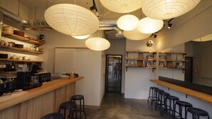 A bar area with wooden counters, black stools, and paper lanterns hanging from the ceiling. - Sunny Day Hostel (Takamatsu)
