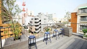 A balcony with three blue bar stools, a wooden planter, and a view of the cityscape. - Sunny Day Hostel (Takamatsu)