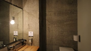 A bathroom with a wooden sink, a hanging light bulb, a mirror, and a toilet.