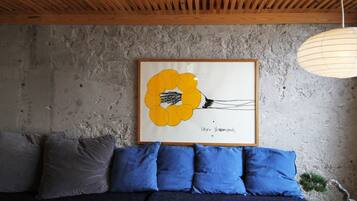 Una habitación con pared de hormigón, una obra de arte enmarcada de una flor amarilla, un sofá azul oscuro con cojines azules y un techo de madera.