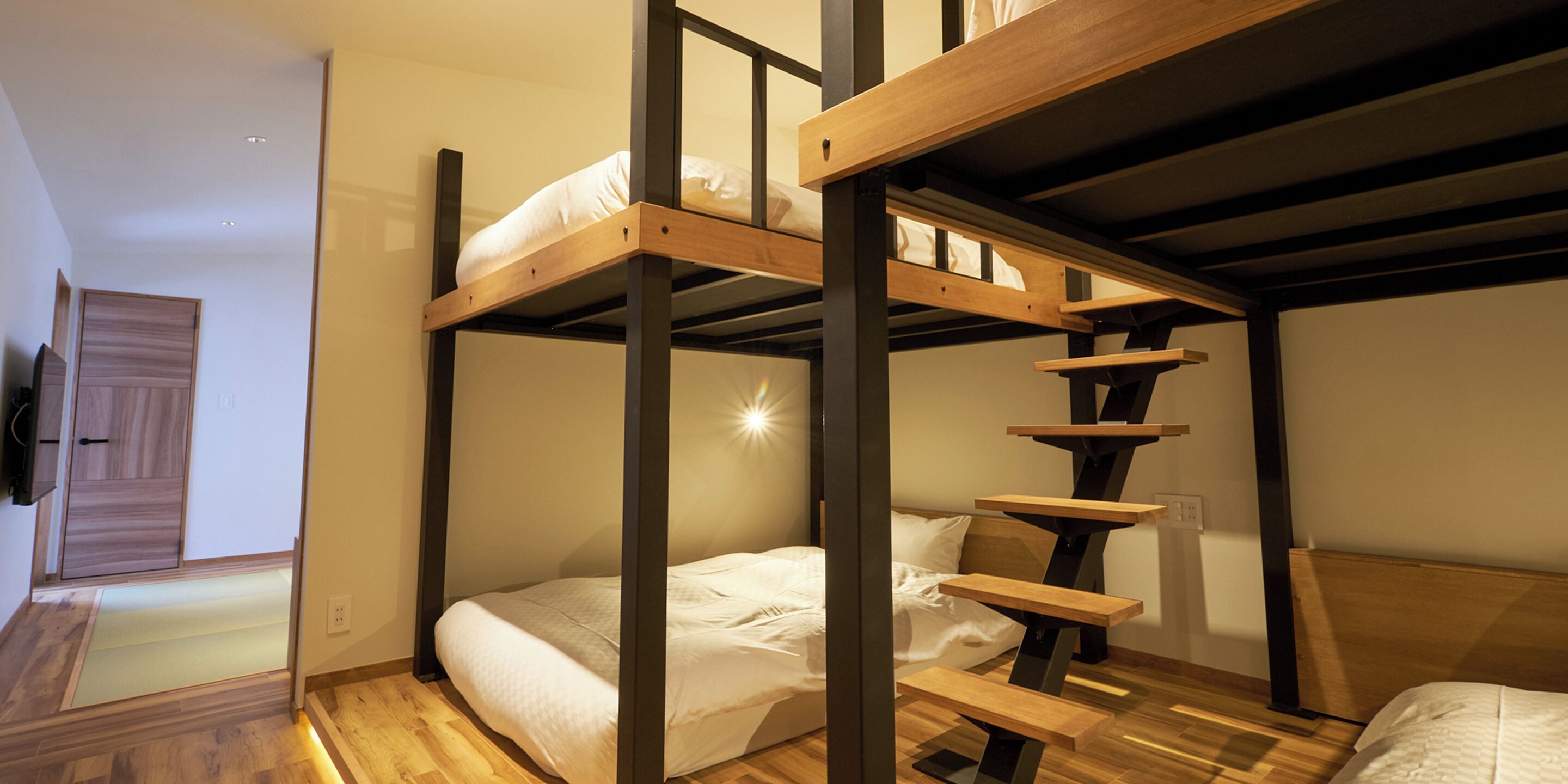 A bunk bed room with a wooden ladder, a wooden door, and a light switch on the wall.