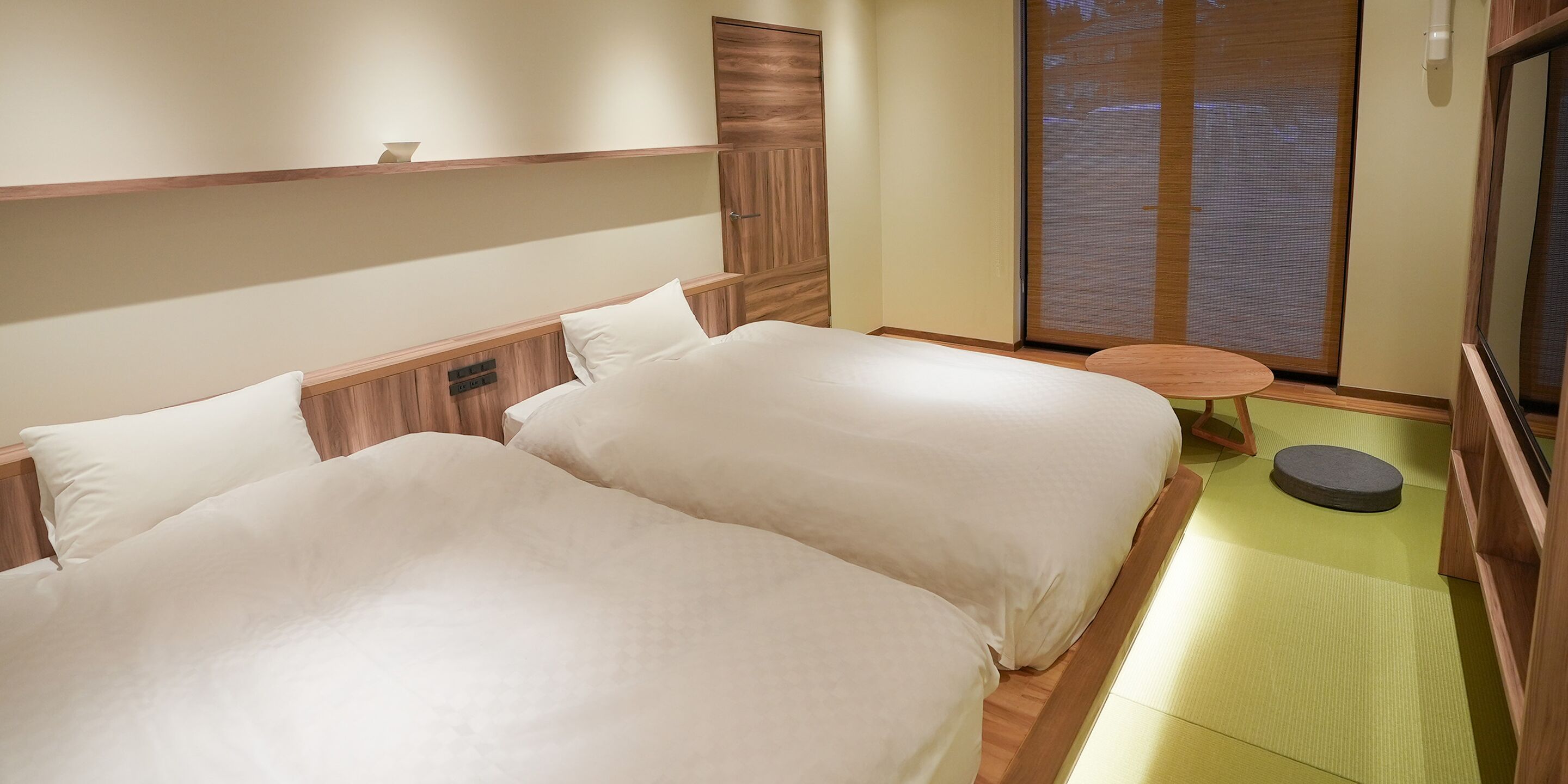 A hotel room with two beds, a small round table, and a sliding door with a view.