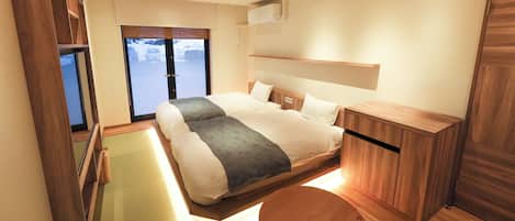 A modern hotel room with a large bed, a wooden nightstand, and a sliding door leading to a balcony.